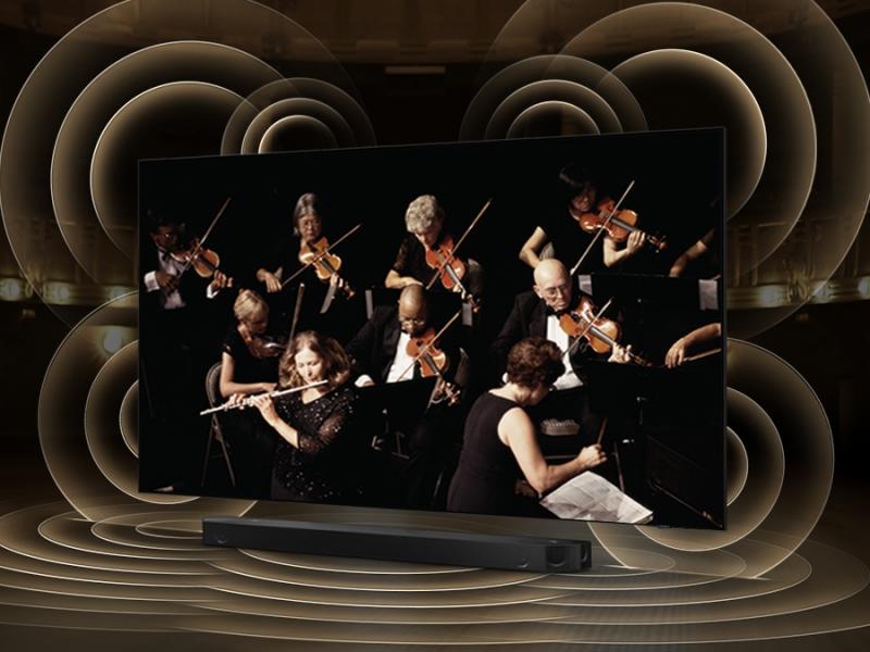 A QLED TV is on top of a Soundbar. Q-symphony is turned on and simulated sound wave graphics from TV and Soundbar demonstrate Q Symphony technology as they play sound together.